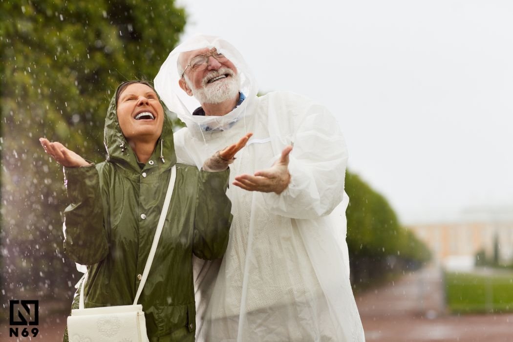 para starszych ludzi w płaszczach przećwideszczowych śmiejących się na deszczu